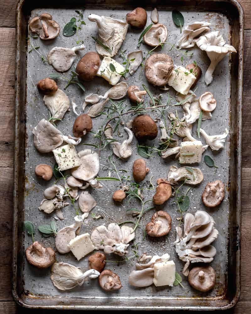 a variety of mushrooms on baking tray with butter and herbs