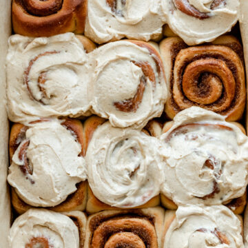 brown butter cinnamon rolls partially frosted in baking dish