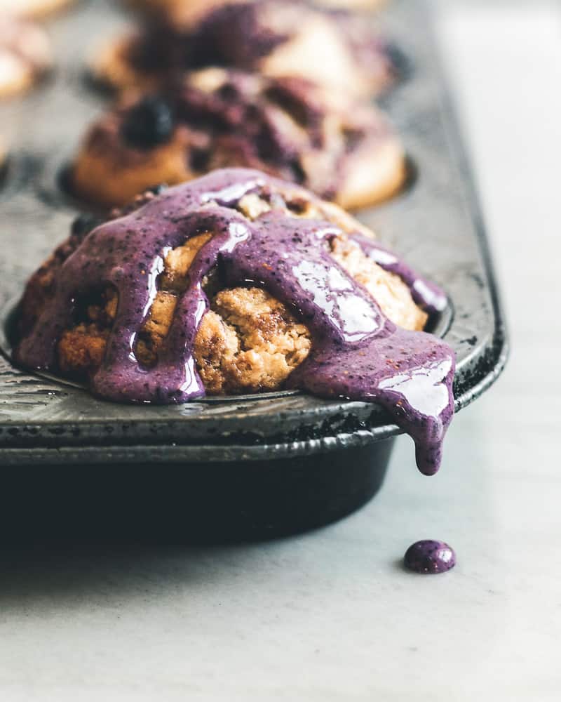 blueberry muffin in muffin tin with purple glaze dripping onto marble surface