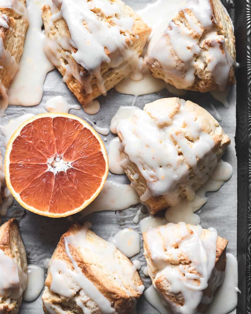 glazed orange scones on baking tray with half of a cara cara orange