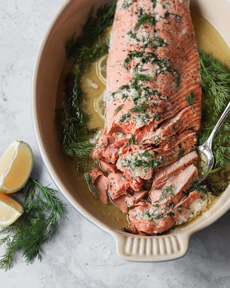 slow roasted salmon in a baking dish surrounded by herbs and lemon