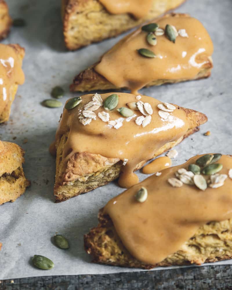 glazed pumpkin scones on parchment lined baking tray with oats and pepitas