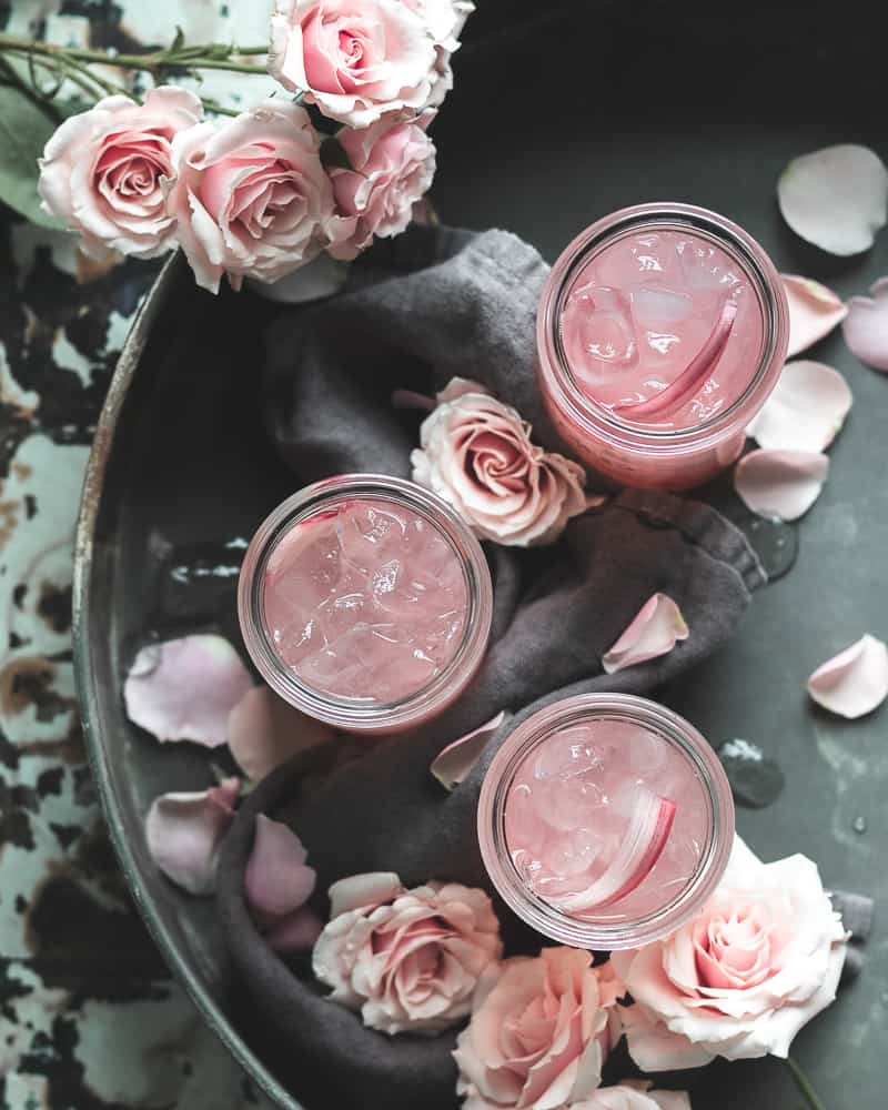 overhead view of 3 rhubarb elderflower refresher cocktails in a metal tray with pink roses