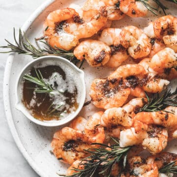 shrimp skewers on white plate with small dish of brown butter