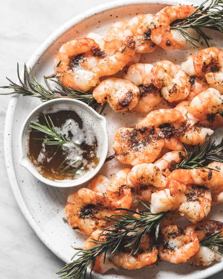 shrimp skewers on white plate with small dish of brown butter