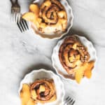 3 peach pecan sticky buns in small white dishes on white marble surface