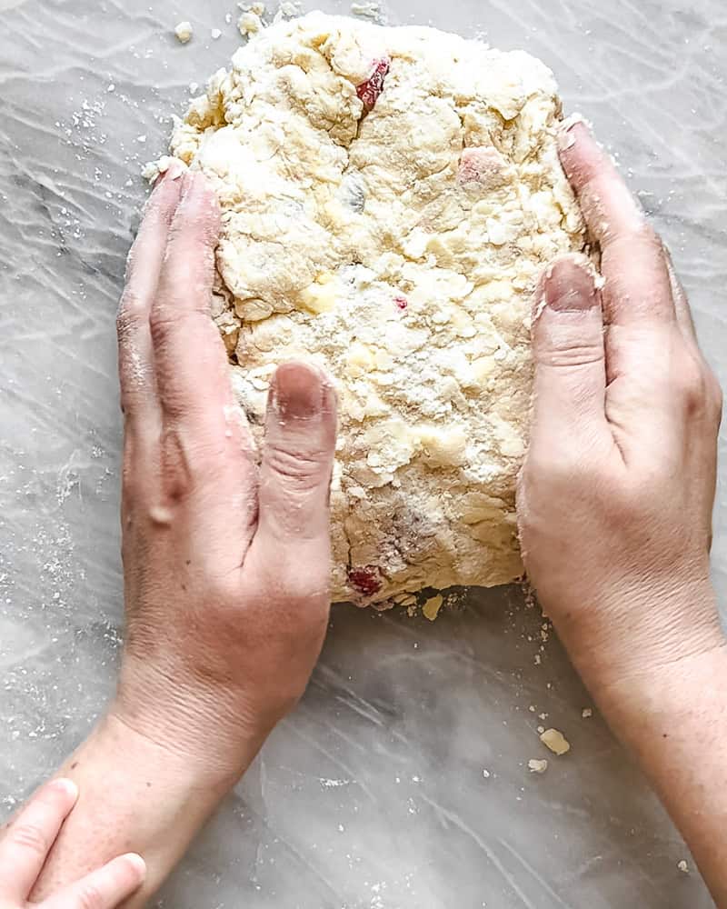 mixed berry scone dough being shaped by hand on marble surface