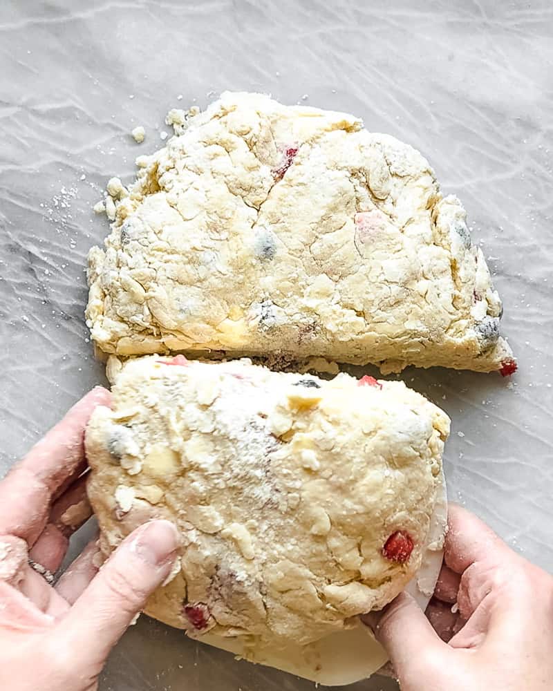 mixed berry scone dough being divided and stacked on white marble surface