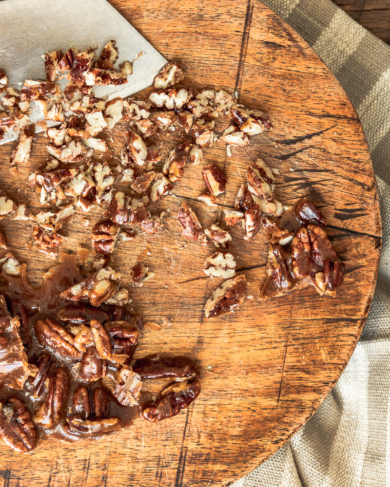 candied pecans on cutting board - some are chopped and some are whole.