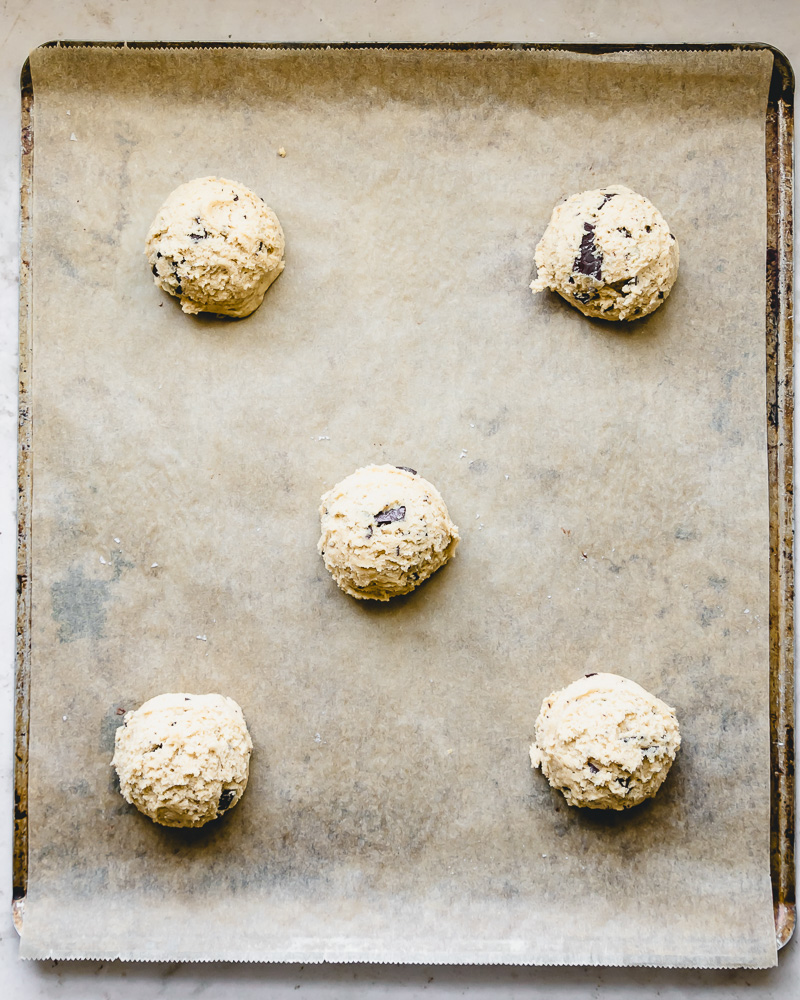 5 cookie dough balls on parchment lined baking sheet