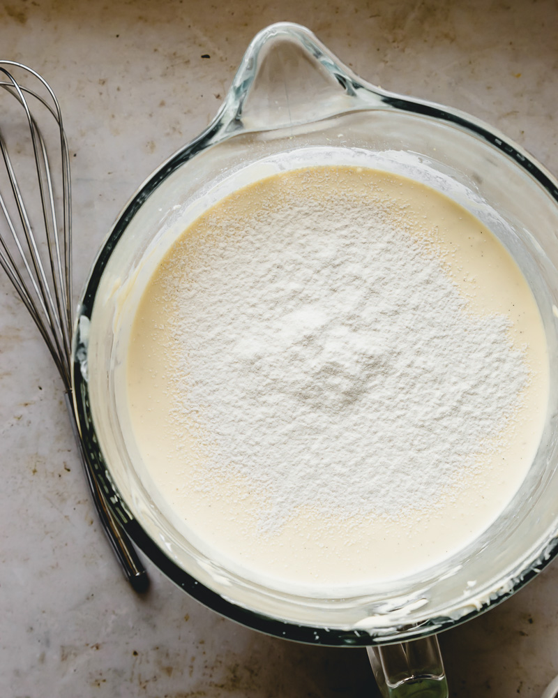 flour sifted on top of cheesecake batter in mixing bowl