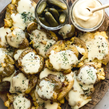 raclette potatoes on round wooden board with small jars of dijon mustard and cornichons