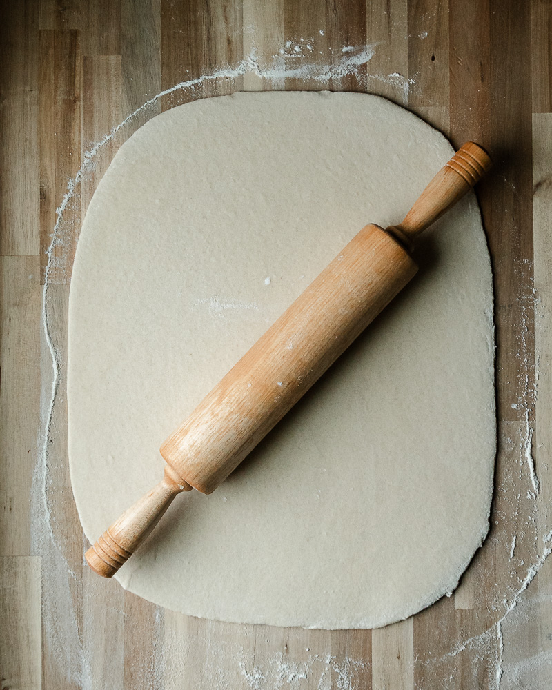 cinnamon roll dough rolled into large rectangle with wooden rolling pin