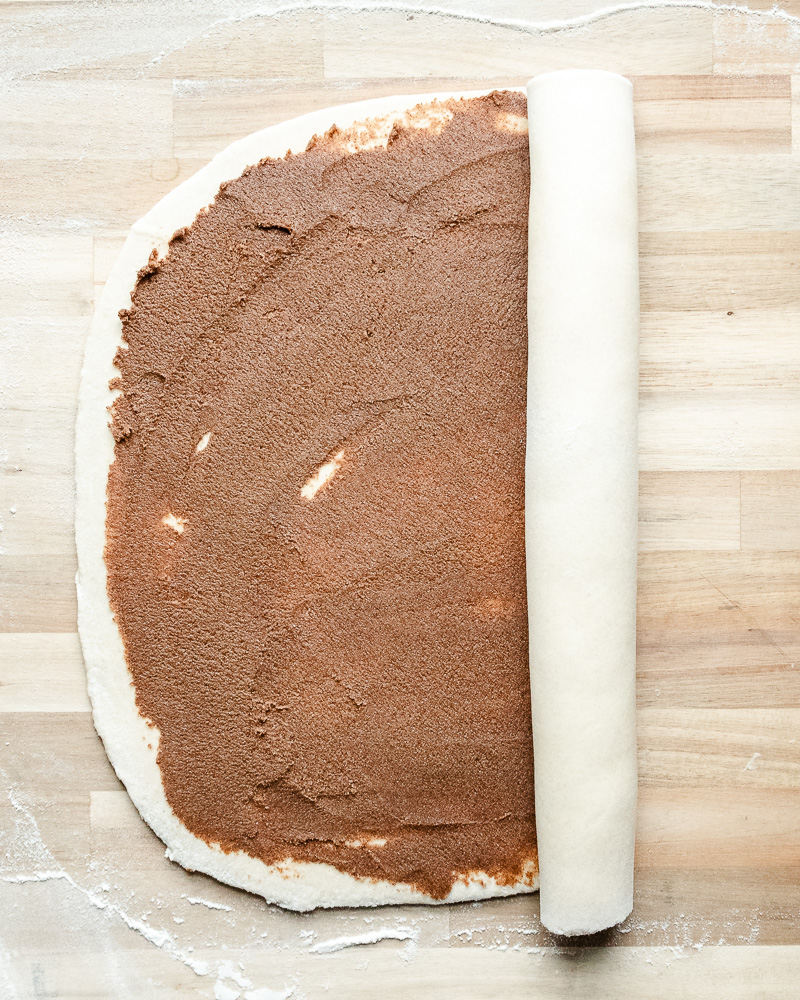 cinnamon roll dough rolled up halfway on wooden surface