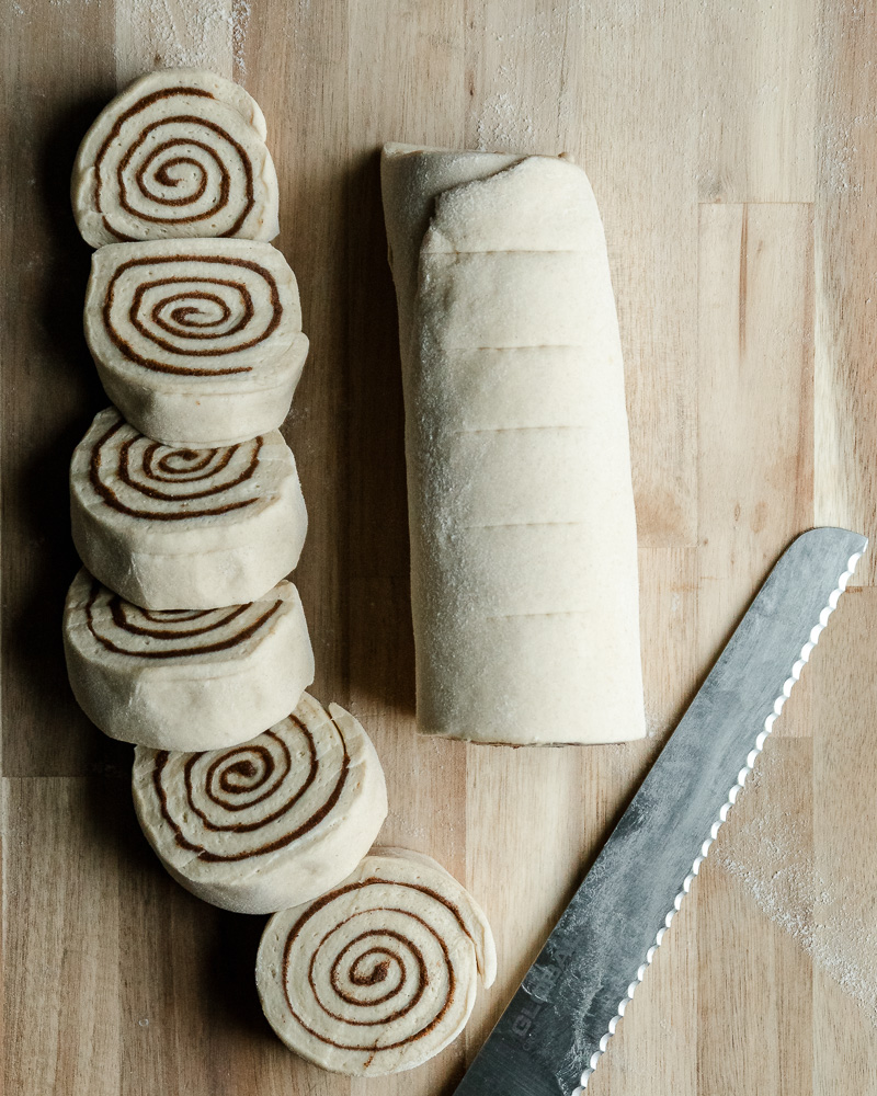 slices of cinnamon roll dough next to half log of unsliced dough and serrated knife