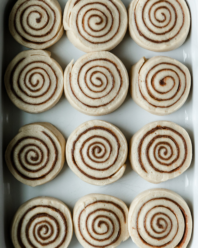 12 cinnamon roll slices in white baking dish after second rise