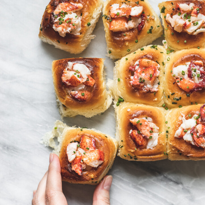 small slider rolls filled with lobster meat with hand reaching in to pull one off