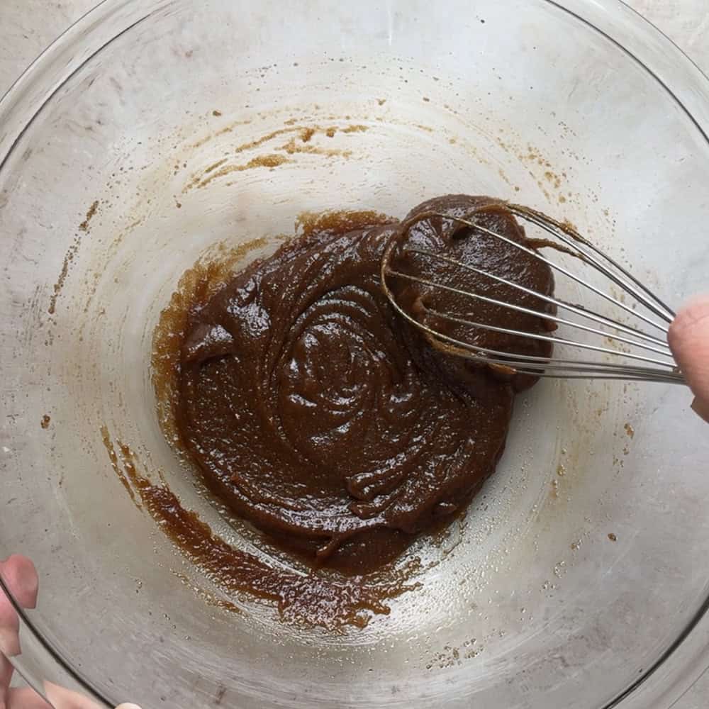 brown sugar and butter mixture being whisked together to form a glossy and cohesive mixture