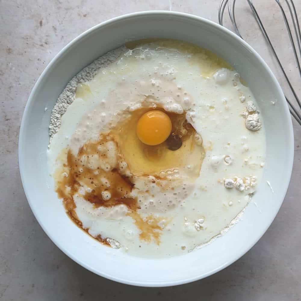 wet ingredients including eggs, sourdough starter, and vanilla, added to dry ingredients in a white mixing bowl