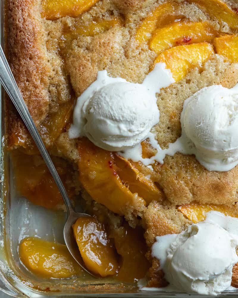 a pan of peach cobbler topped with 3 scoops of ice cream with one corner scooped out