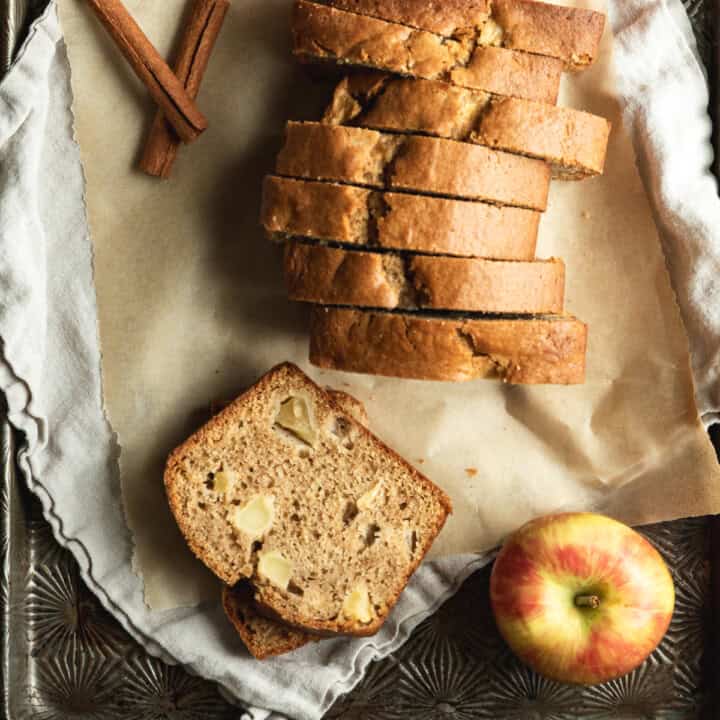 overhead image of sliced apple bread on baking tray with fresh apples and cinnamon sticks
