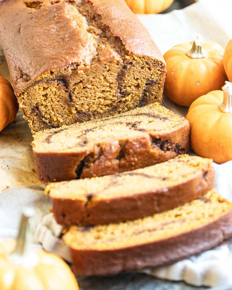 sliced pumpkin bread on tray with miniature pumpkins