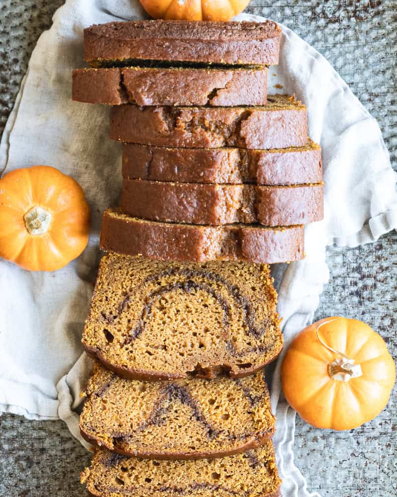 overhead image of sliced pumpkin bread on tray with linen napkin and miniature pumpkins