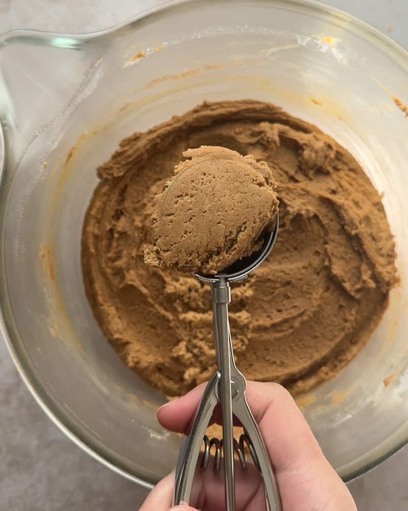 cookie dough in a metal cookie scoop with bowl of dough underneath