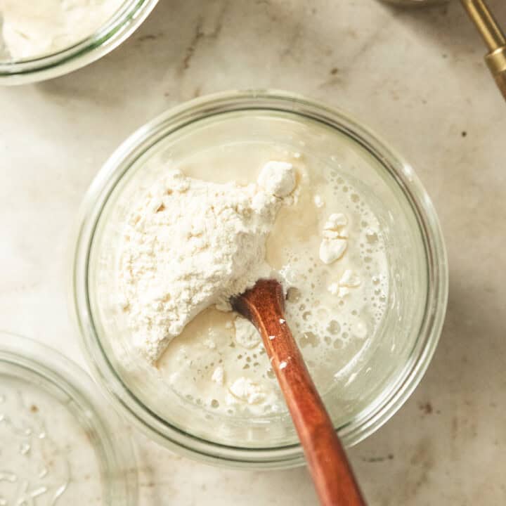a glass jar with flour and water and a wooden spoon inside