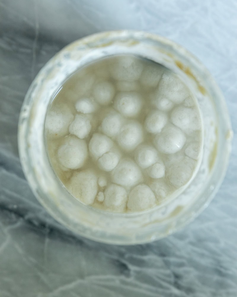 overhead view of a jar of sourdough starter with hooch volcanoes on the surface