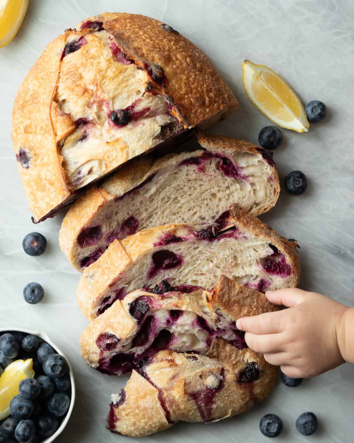 a loaf of sliced blueberry bread with a little hand reaching in grabbing one slice