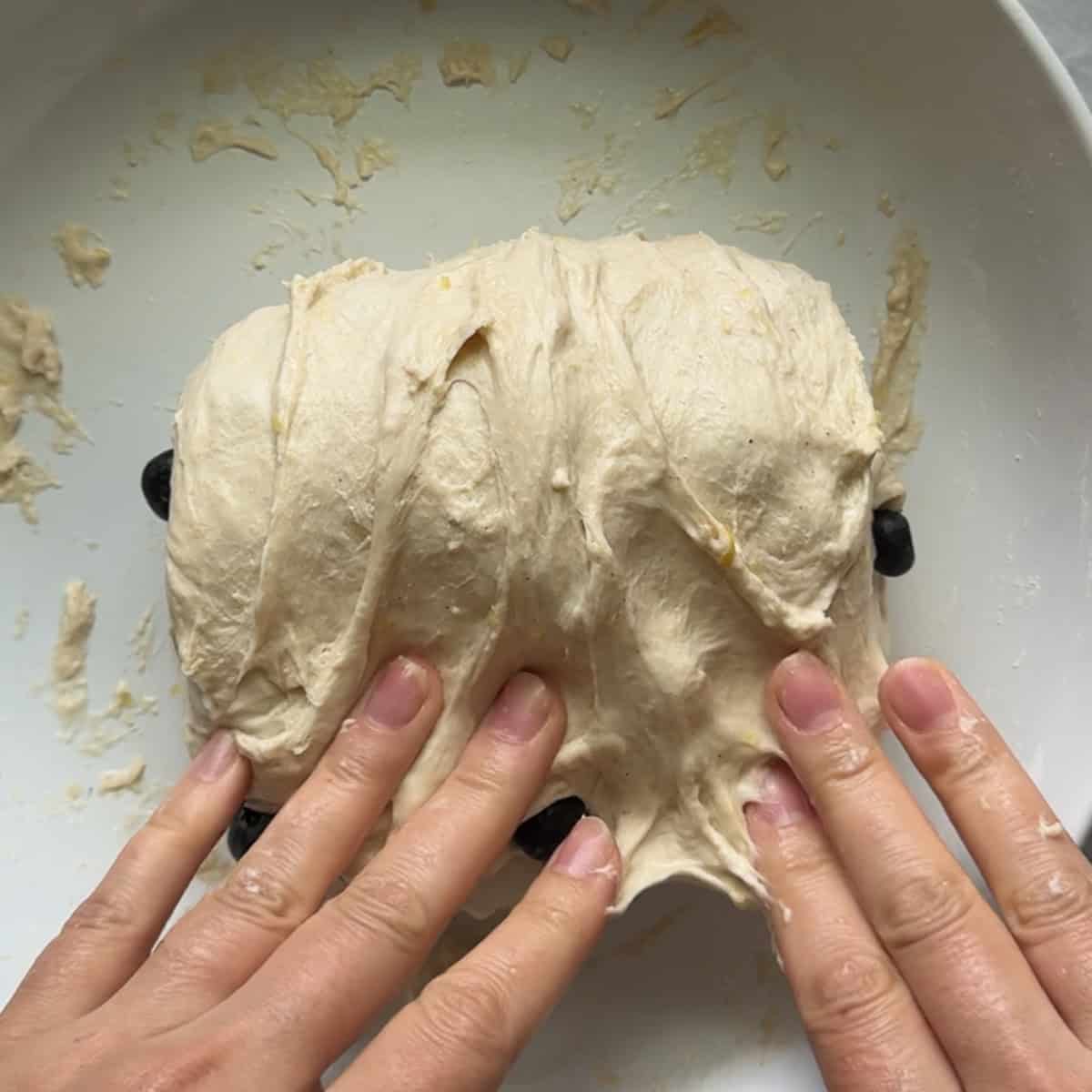 dough being folded over itself in white bowl
