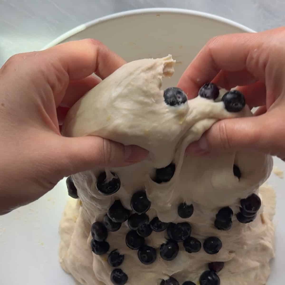 dough full of blueberries being pulled up and over itself in white bowl