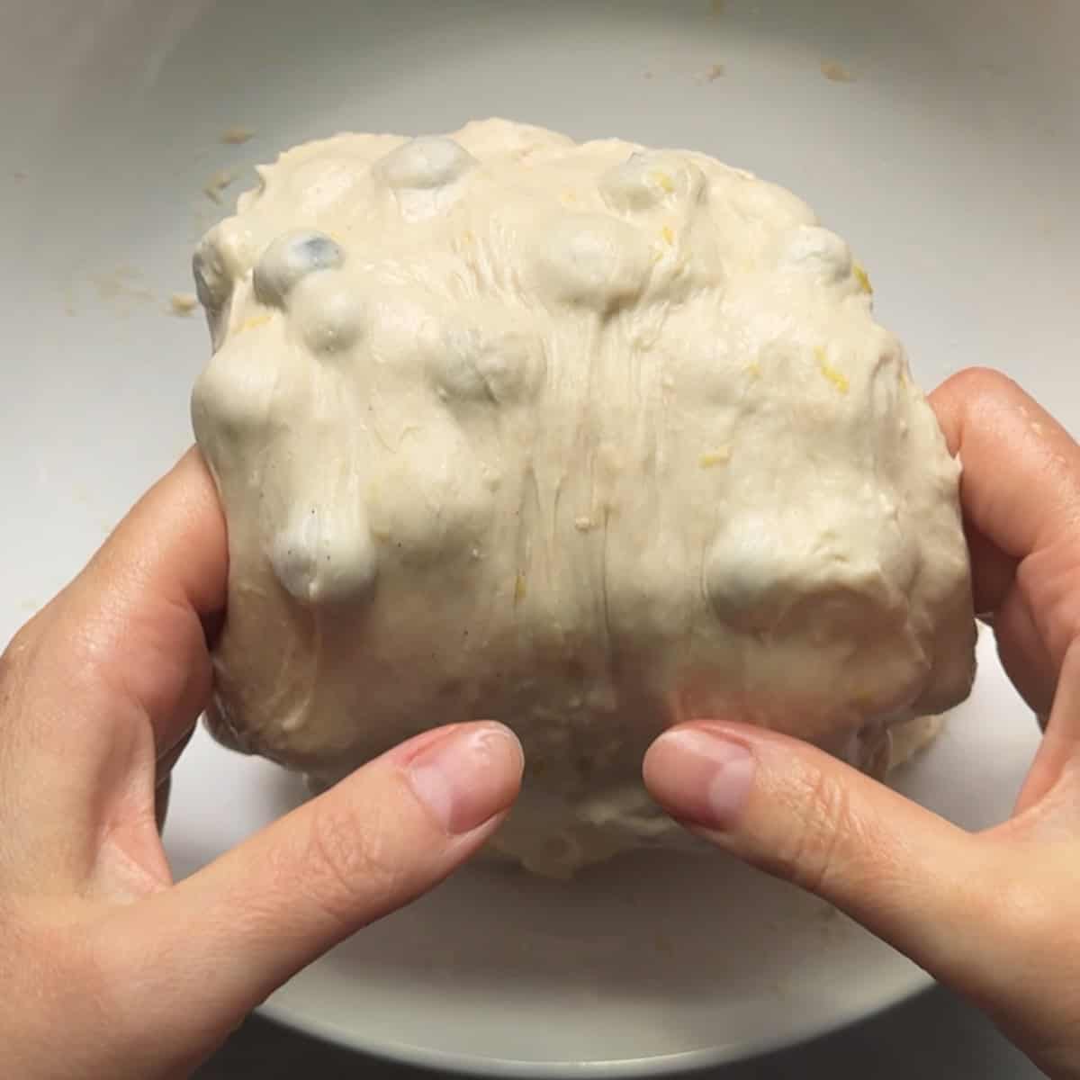 dough being lifted up and out of bowl by hand to perform a coil fold