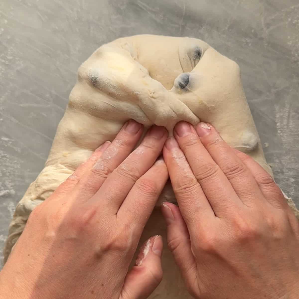 sides of dough being pulled in to create a loaf shape
