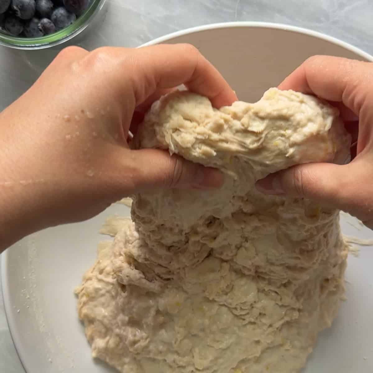 dough being stretched up out of a white bowl by two hands