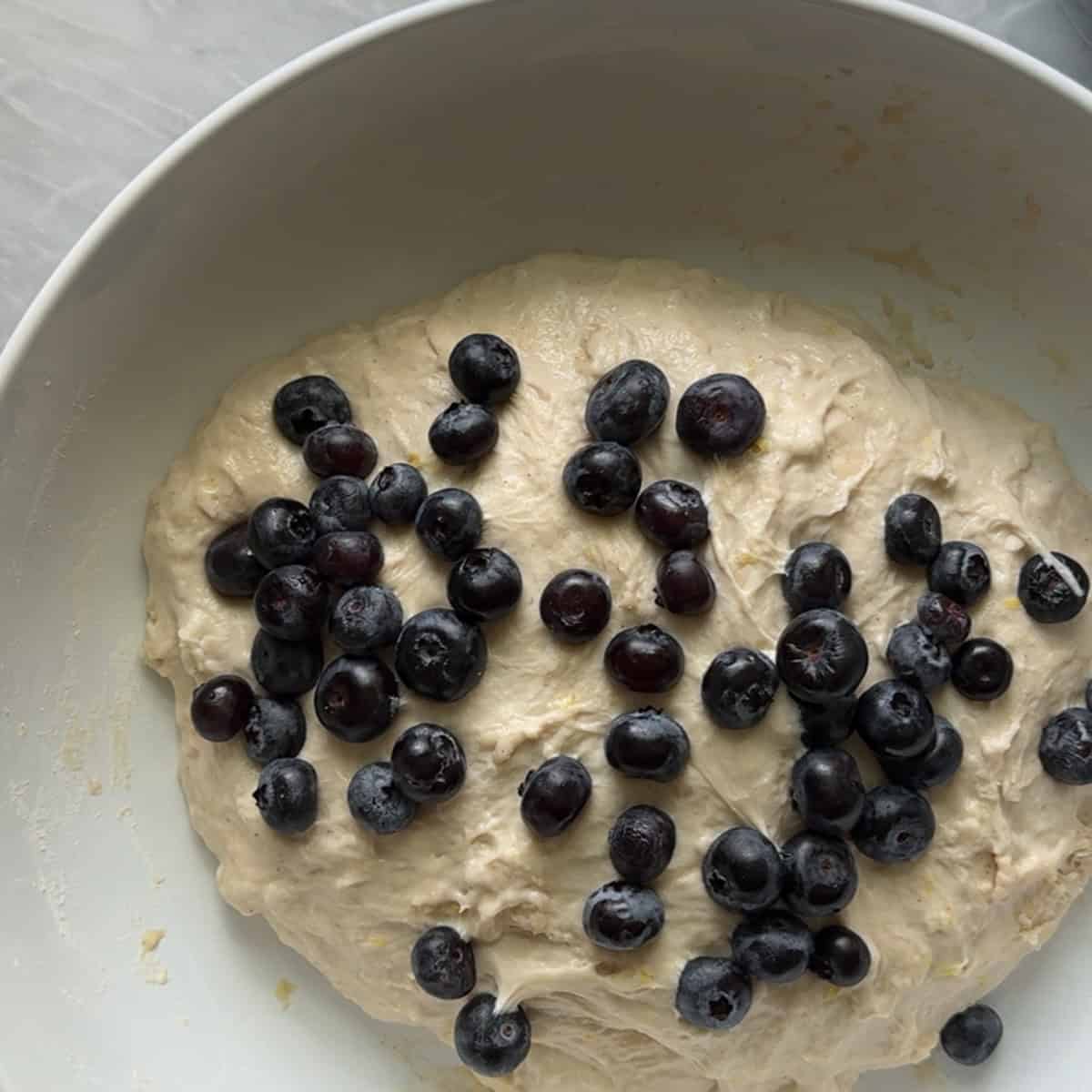 fresh blueberries added to dough in white bowl