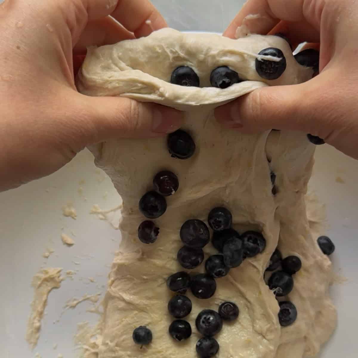 Dough with blueberries being stretched up and over itself by hand