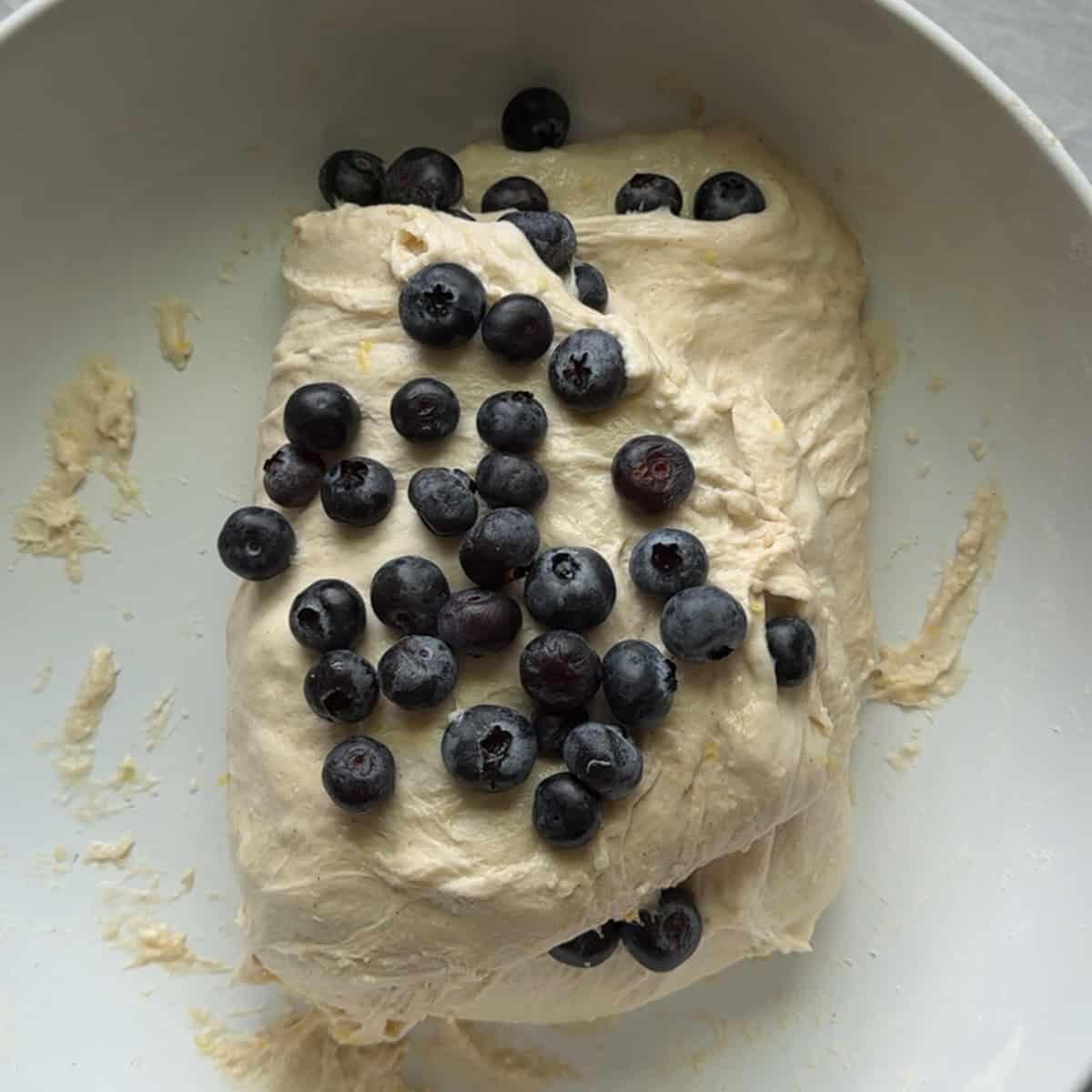 fourth layer of blueberries added to top of bread dough in white bowl