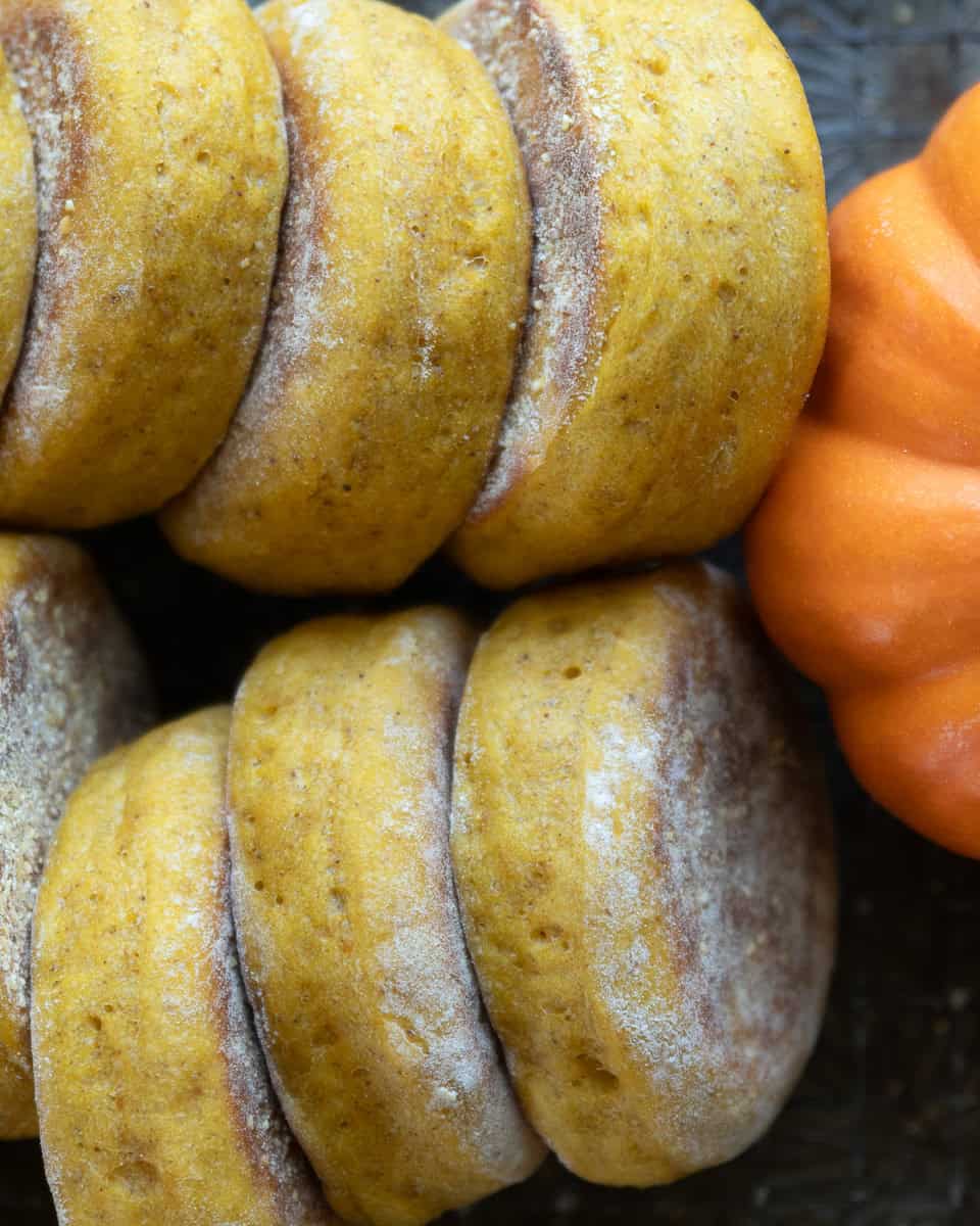 Pumpkin English Muffins lined up on their sides leaning against a small orange pumpkin