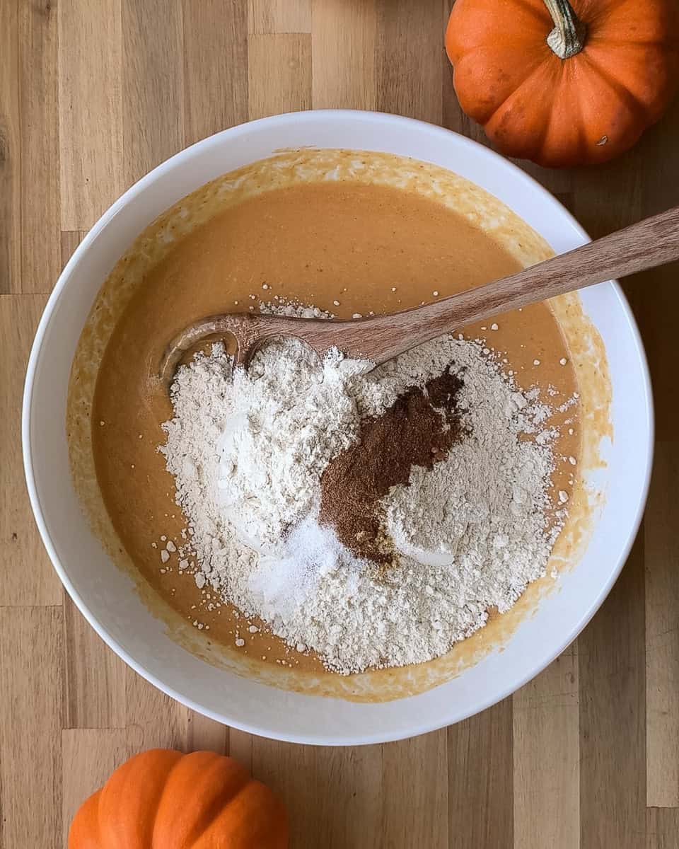 Dry ingredients including flour and spices added to wet mixture in white bowl
