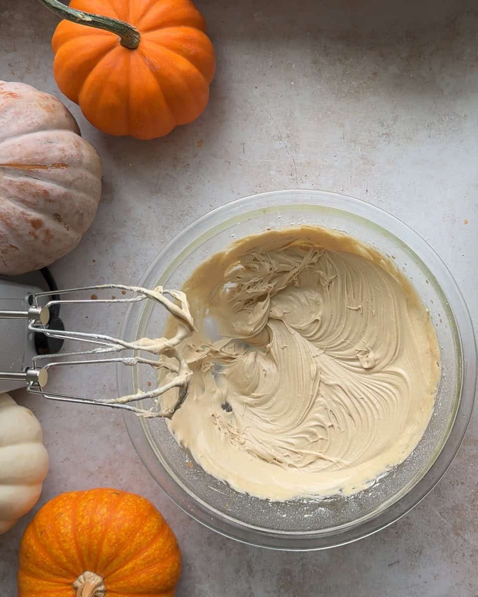 frosting in glass bowl next to pumpkins and hand mixer