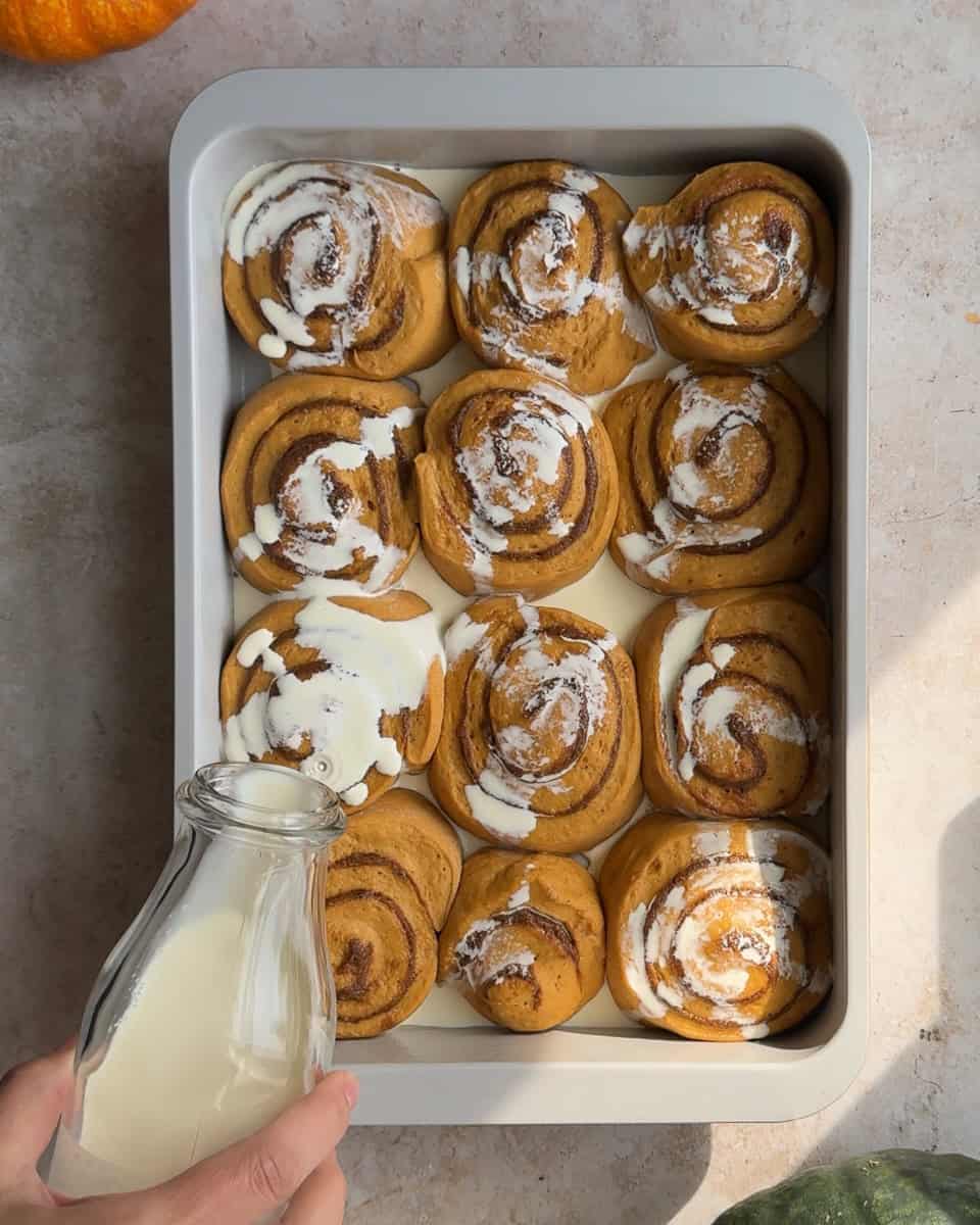 cream being drizzled on cinnamon rolls before baking